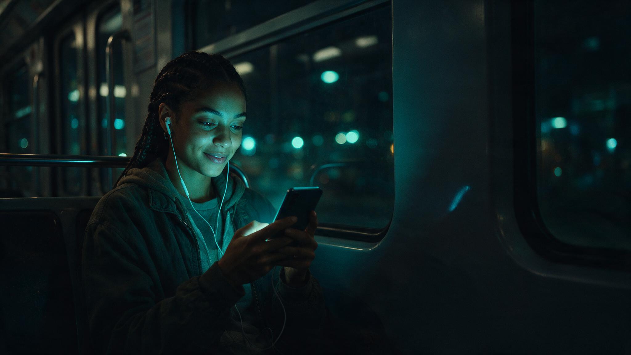 Pessoa assistindo a um vídeo no celular, tela iluminada em ciano, ilustrando o consumo de conteúdo audiovisual no dia a dia.